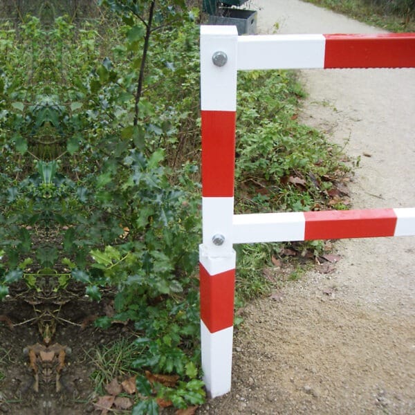 PARAT Gatterschranke mit roten und weißen Streifen am Rand eines Schotterwegs, umgeben von grünen Büschen und Pflanzen.