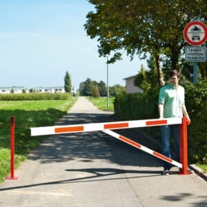 Eine Person steht an einer abgesenkten rot-weißen COMPACT Drehschranke auf asphaltiertem Feldweg mit Verkehrsschild.