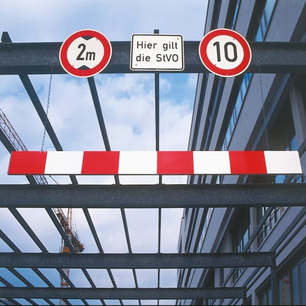 Rote-weiße MORION Aluminium Höhenbegrenzer Schranke mit 2m Durchfahrtshöhe und 10 km/h Schild am Gebäude-Eingang.
