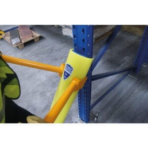 Gelber Rammschutz für Lagerregal aus Metall am blauen Regalpfosten, orange Sicherheitsgeländer, Paletten im Hintergrund.