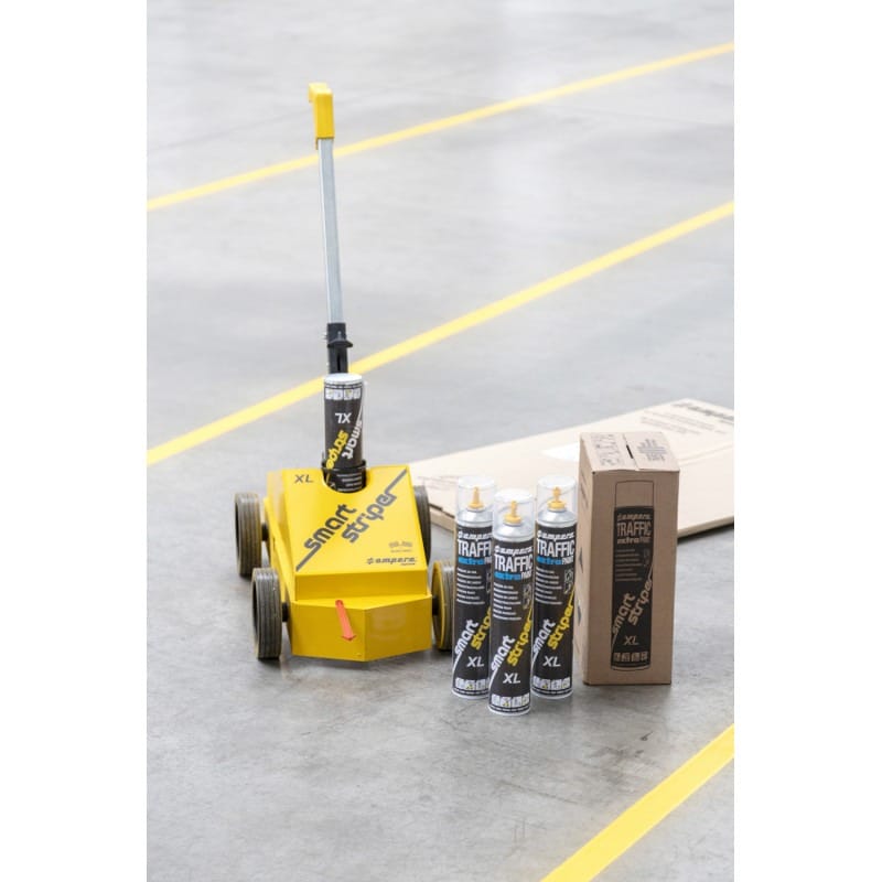 Das Traffic Extra Lack-Set mit KT und Perfekt Striper steht auf gelbem Linienboden, fünf Spraydosen und Karton daneben.
