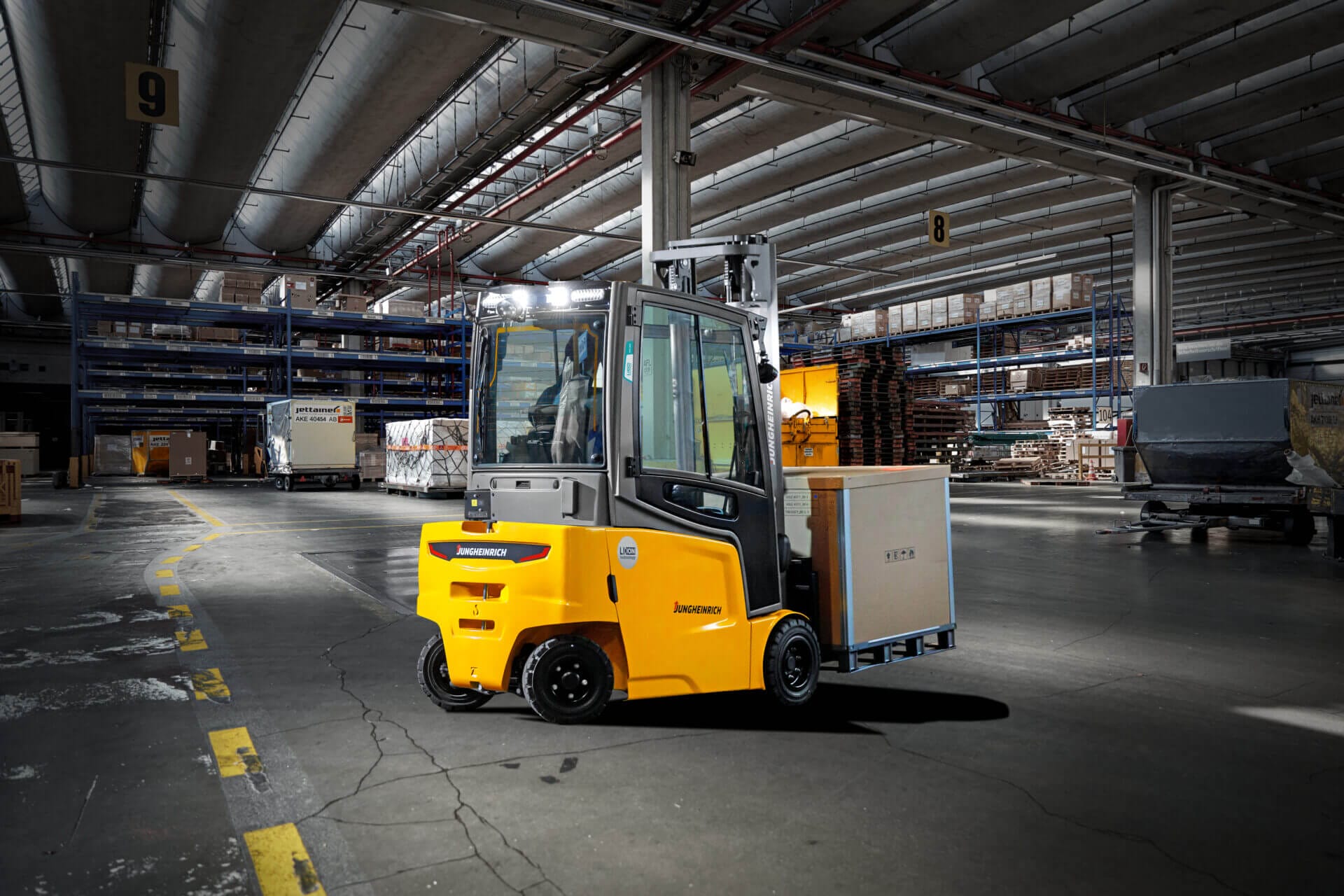 Gelber Gabelstapler fährt mit Palettenboxen durch große Lager mit hohen Decken und industriellen Regalen.