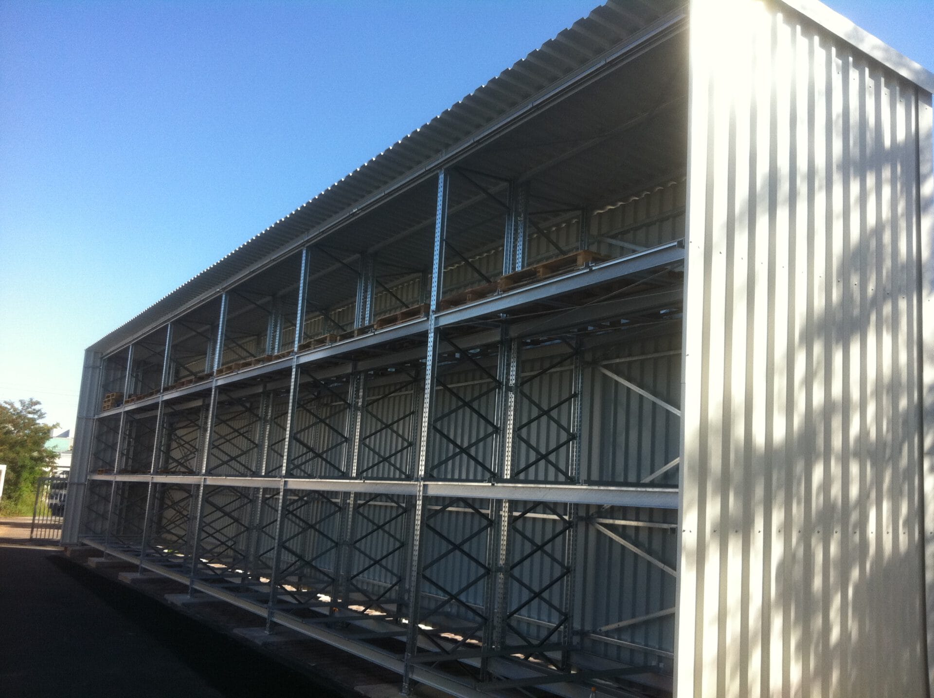 Großes leeres Metallregal in mehrstöckiger Wellblechhalle, aus Winkel mit Fokus auf Regalgröße und Stahlkonstruktion fotografiert.