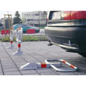Ein Auto steht auf gepflastertem Boden vor drei SESAM-privat Parkplatzbügeln aus Metall mit rot-weißen Streifen.