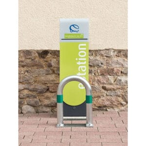 Grüne und weiße E-Ladestation auf Pflastersteinen vor Steinmauer, davor CITY-Schutzbügel KLEIN Fahrradständer.