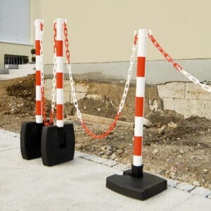 Drei Ketten-Warnständer mit Kunststoffketten versperren den Zugang zu einer Baustelle neben einem Gebäude.