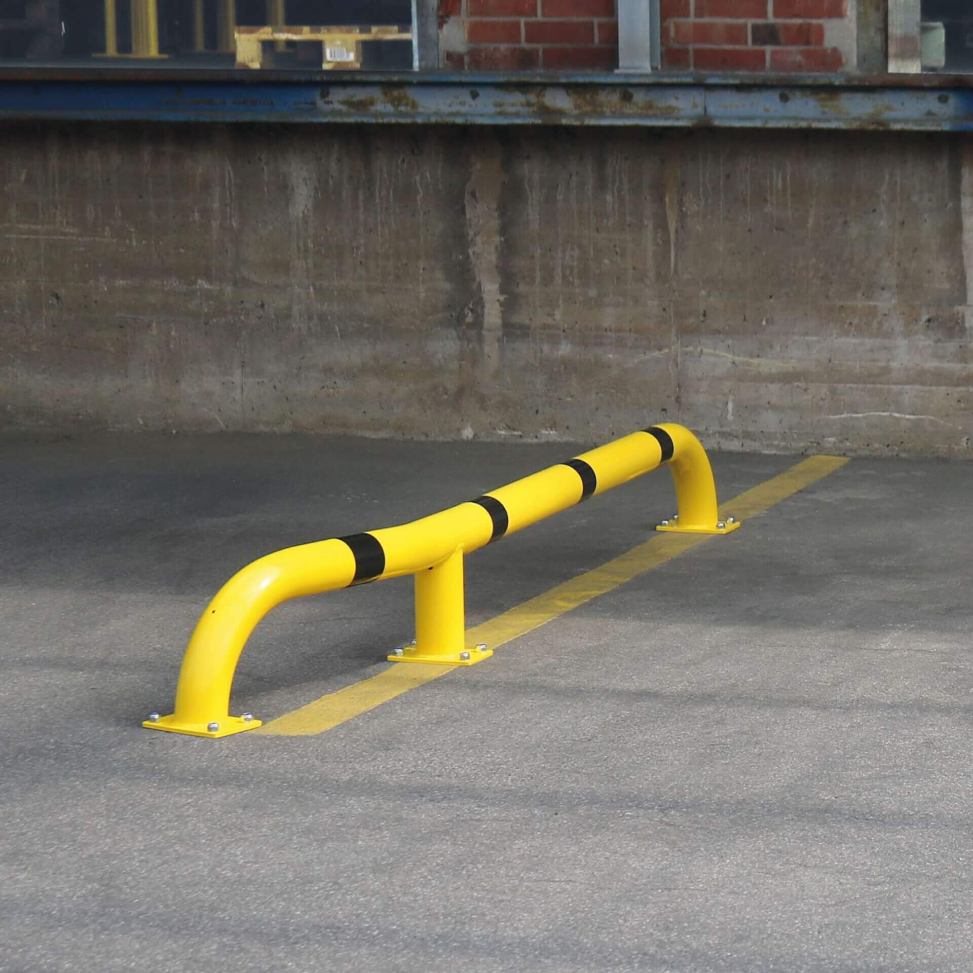 Gelbe BLACK BULL LKW-Einfahrhilfe aus Metall mit schwarzen Streifen steht auf Asphalt vor einer Beton-Laderampe.