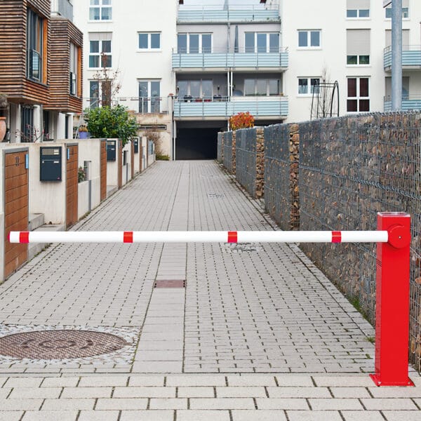 Kompakte Elektroschranke mit Solarmodul sperrt eine asphaltierte Einfahrt, umgeben von modernen Wohngebäuden und Zäunen.
