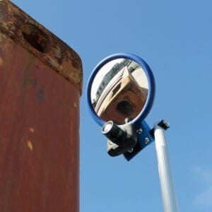 Runder Inspektionsspiegel mit blauem Rahmen und LED-Licht spiegelt rostige Metalloberfläche vor klarem Himmel.