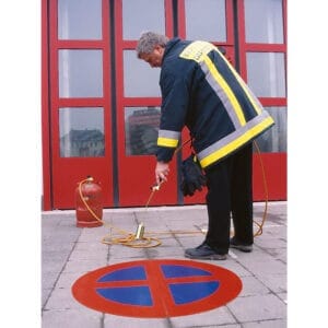 Feuerwehrmann bringt mit PROline-Thermo-Klebefolie und Brenner Halteverbot-Symbol auf Gehweg vor Gebäude mit roten Türen an.