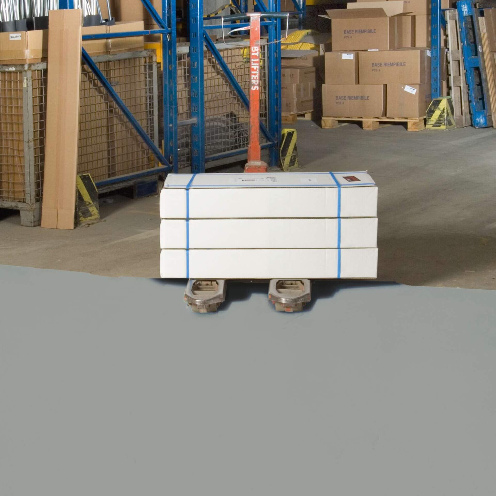 Hubwagen mit vier weißen PROline-Paint Hallenmarkierfarbe Boxen auf Lagerboden, umgeben von Metallregalen und Kartons.