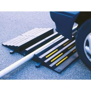 Autoreifen überquert MORION-Schlauchbrücke mit gelben Streifen, schützt Stromkabel auf Asphaltboden vor Beschädigung.