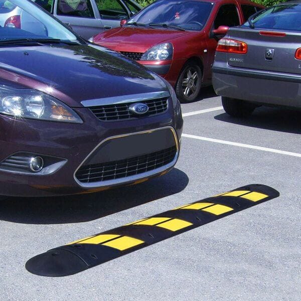 EasyRide Fahrbahnschwelle mit schwarz-gelben Streifen, montiert auf Parkplatz, mehrere Autos im Hintergrund sichtbar.