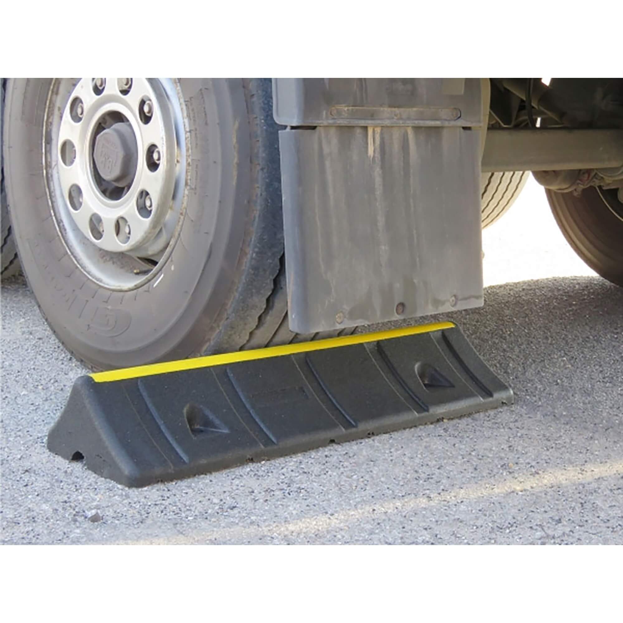 Lkw-Reifen wird von MORION Radstopp Heavy Duty, schwarzer Gummi-Parkbalken mit gelbem Streifen, auf Asphalt gestoppt.