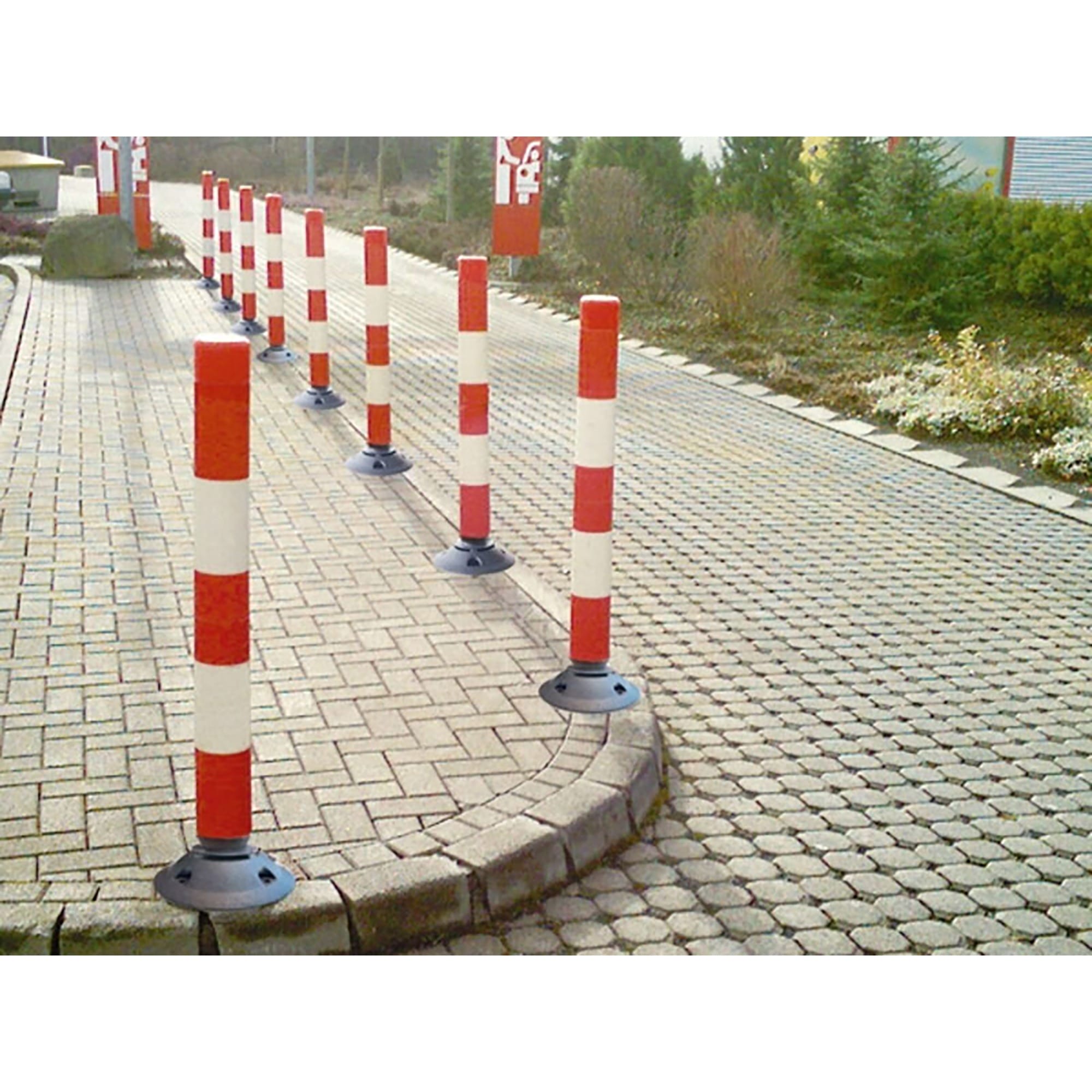 Leitpfosten rot-weiß gestreift grenzen den asphaltierten Gehweg von begrünten Flächen entlang des Wegs deutlich ab.