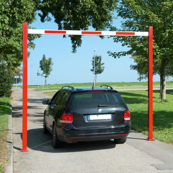 Schwarzer Kombi unter COMPACT Durchfahrtbegrenzer starr, rot-weiße Höhenbegrenzung, Asphaltstraße, Bäume und Gras.