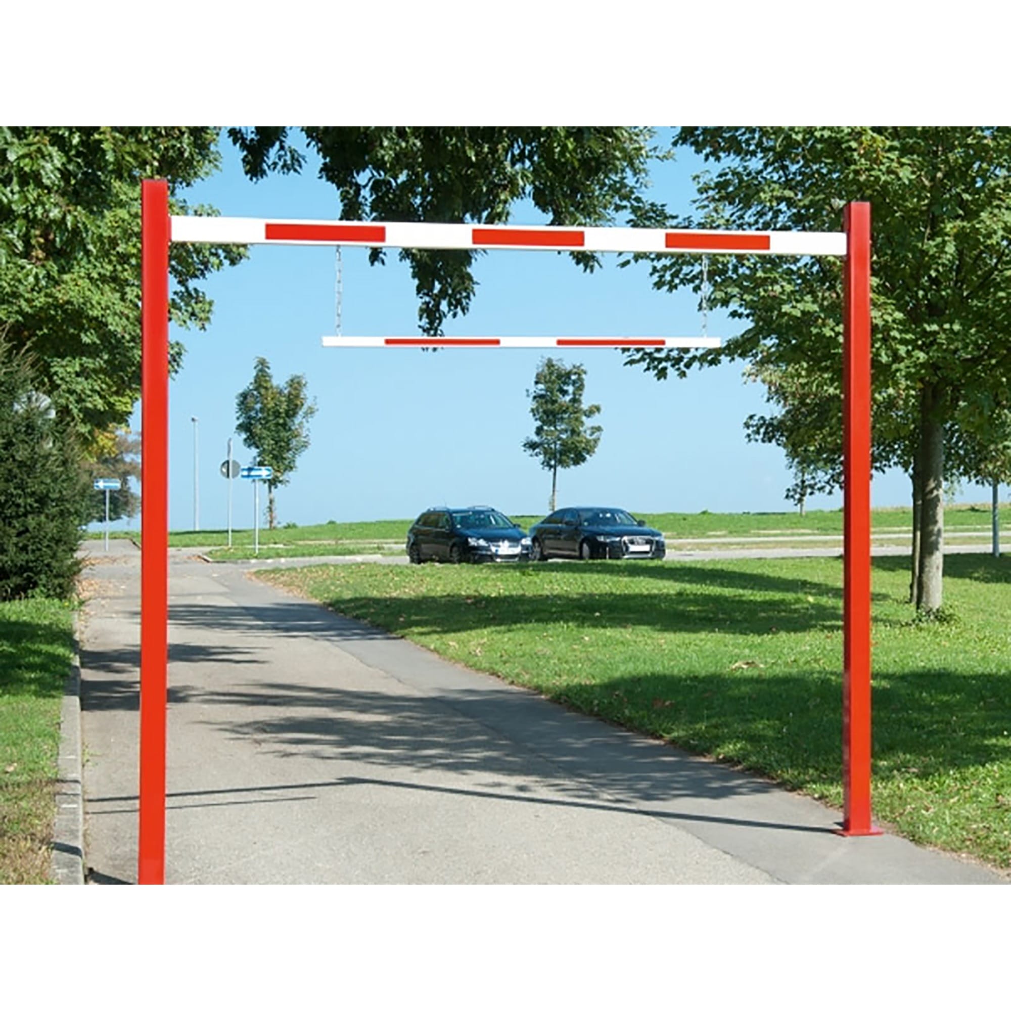 Rote-weiße Durchfahrtbegrenzer barriere über gepflastertem Weg, im Hintergrund Rasen, Bäume und geparkte Autos.