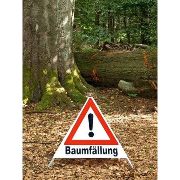 Trio-Faltsignal mit Ausrufezeichen und "Baumfällung" steht im Wald neben einem großen umgestürzten Baum.