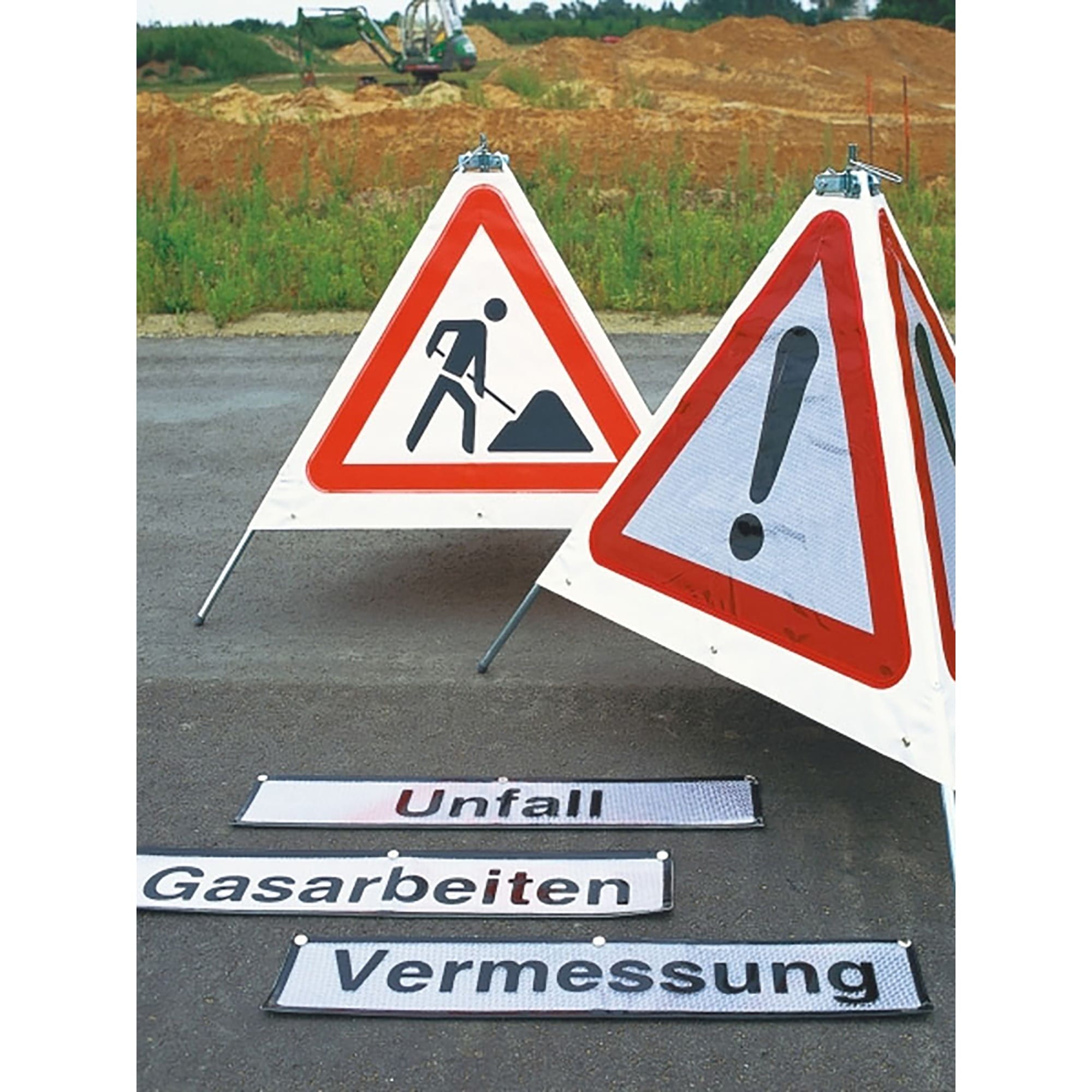 Zwei dreieckige Baustellen-Warnschilder mit Aufschrift Unfall, Gasarbeiten, Vermessung auf Asphalt vor Baustelle sichtbar.