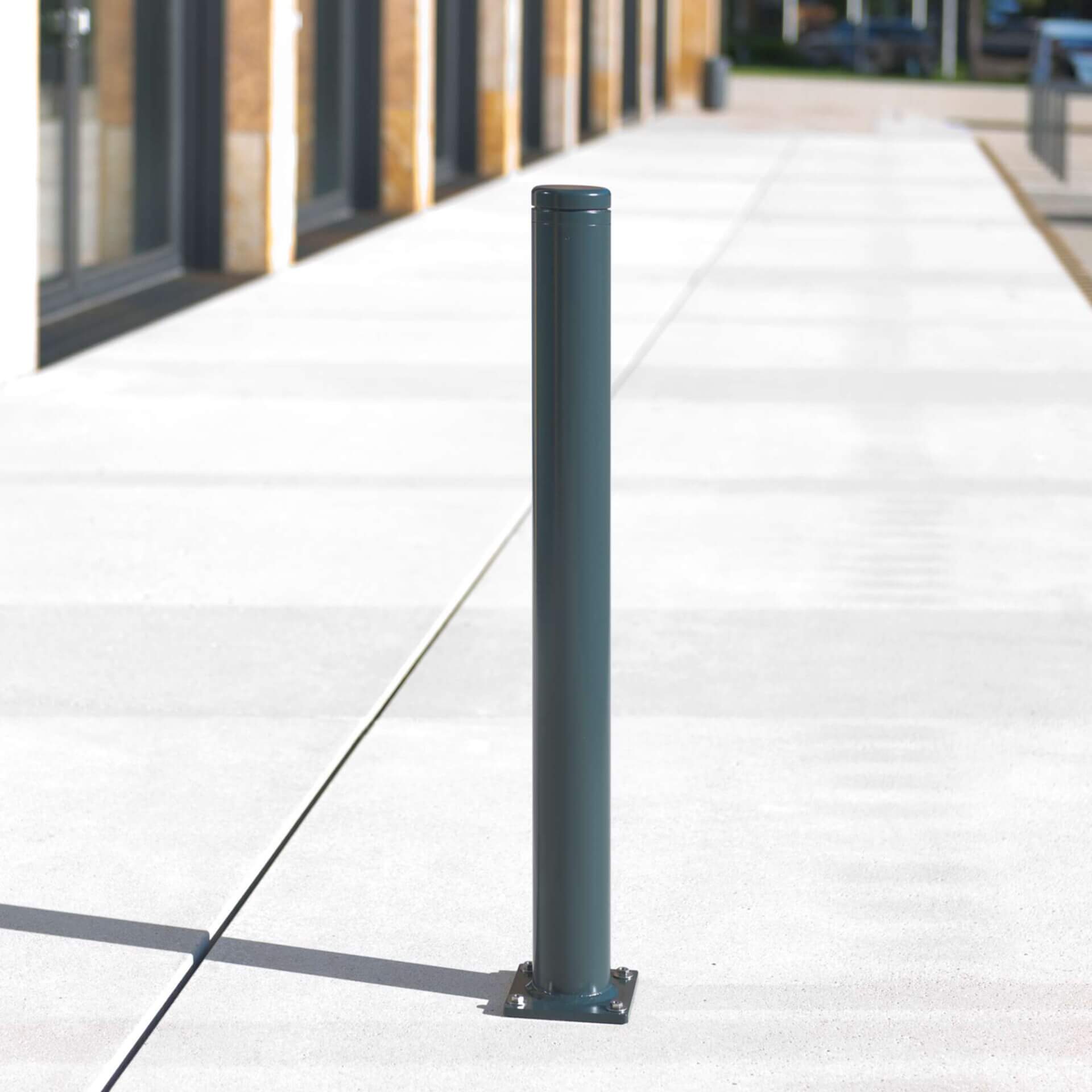 Ein dunkelgrauer Metall-Poller City-Poller LEIPZIG steht auf hellem Beton-Bürgersteig vor einem Gebäude in Leipzig.