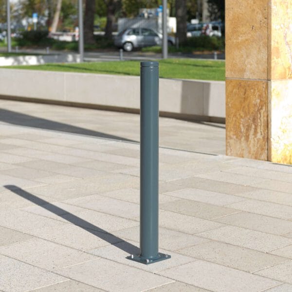 Stadtpoller Leipzig aus grauem Metall auf gepflastertem Gehweg neben beigem Steinsockel und grünem Rasen.