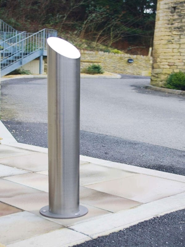 CITY-Poller BERLIN 45 Edelstahl Pollerleuchte auf Pflaster an Straße, neben Steinmauer, Treppe und Grünfläche im Hintergrund.