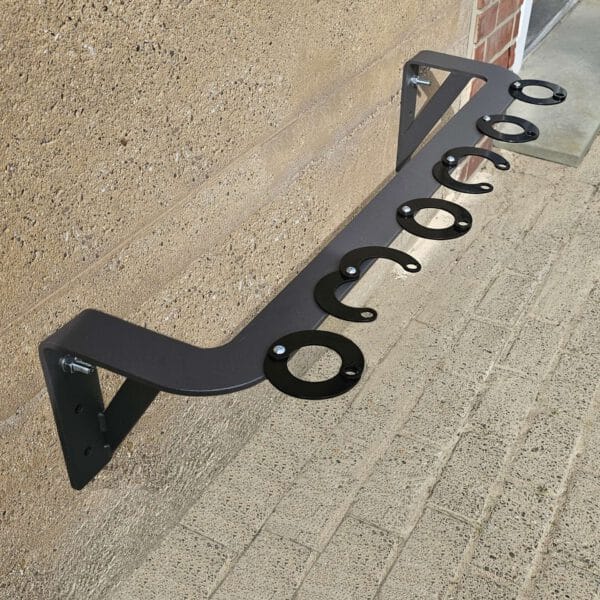CITY-Scooter-Parker GILA Metallständer mit mehreren runden Haltern, an Ziegelwand auf gepflasterter Fläche montiert.