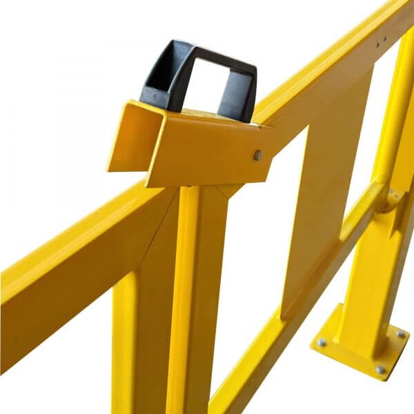 Detailaufnahme eines gelben U-förmigen Stahlriegels mit schwarzem Kunststoffgriff und verschraubter Metall-Bodenplatte.