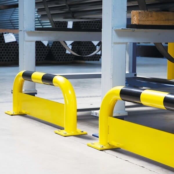 Gelb-schwarzer BLACK BULL Rammschutz-Bügel mit Unterfahrschutz montiert auf Betonboden, schützt Industrie-Metallregale.
