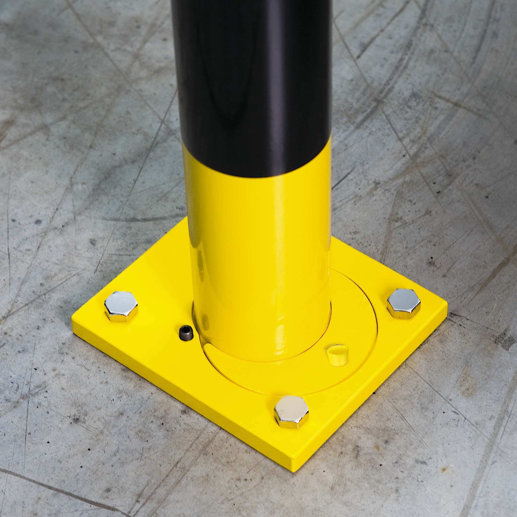 Gelb-schwarzer Rammschutzbügel, abnehmbar, befestigt mit vier großen Schrauben am Betonboden; Schutzpoller für Lager.