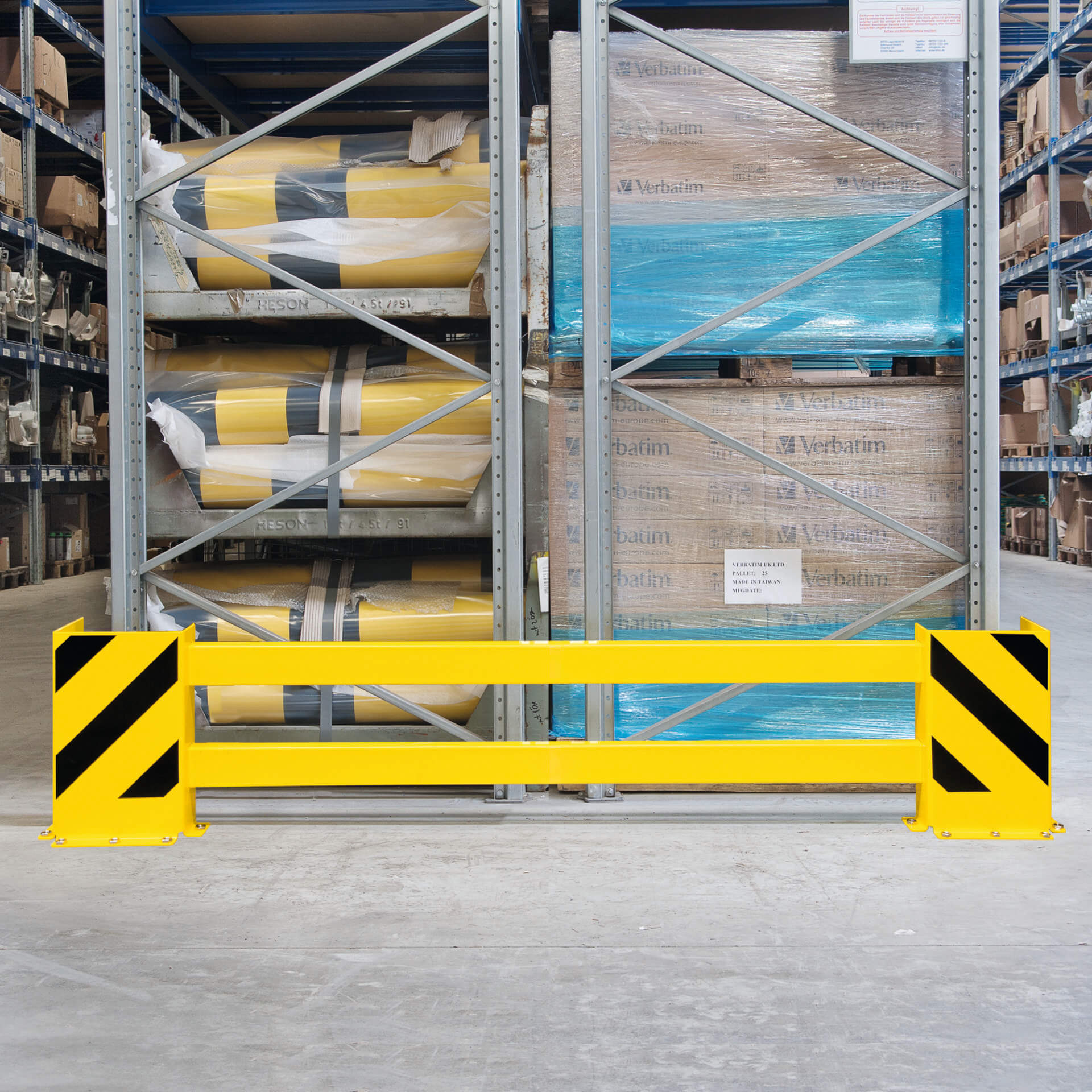 Gelb-schwarze BLACK BULL Regalschutz-Planke vor Lagerregalen mit Paletten und Materialrollen als Anfahrschutz montiert.