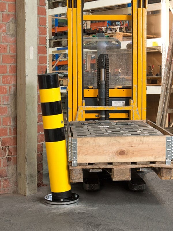 Gabelstapler mit Holzpalette fährt auf BLACK BULL Rammschutz-Poller SWING drehbar im Industrie-Lager zu.