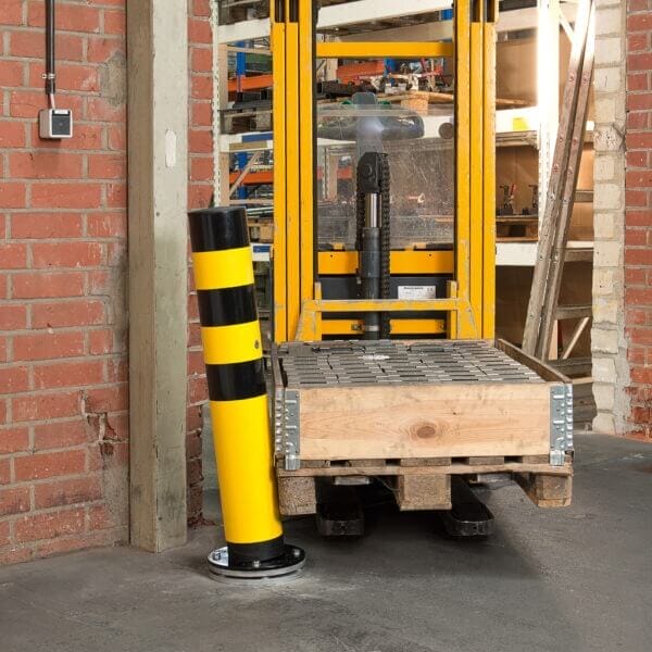 Gelber Gabelstapler transportiert Ziegelpalette neben BLACK BULL Rammschutz-Poller SWING drehbar in Lagerhalle.