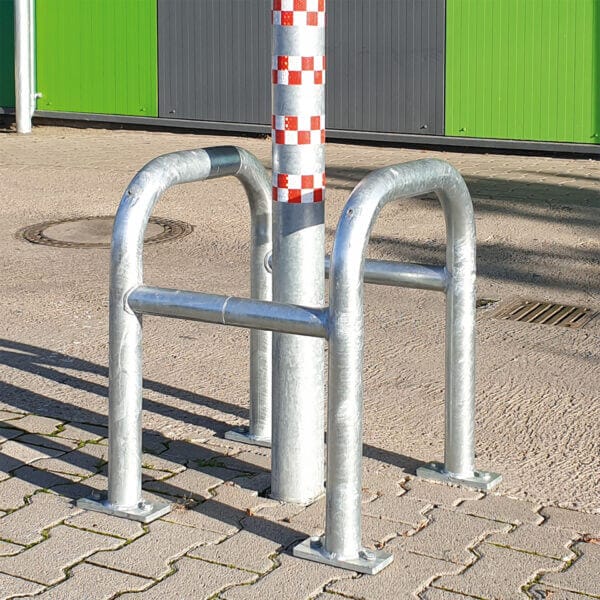 Silberner MORION Säulenschutz umgibt einen Metallpfosten mit rot-weißer Schachbrettmarkierung auf Pflasterfläche.