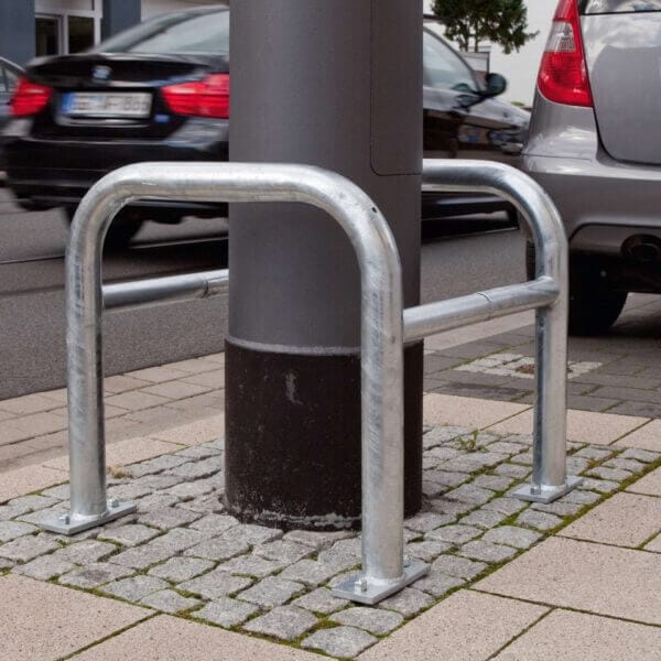 MORION Säulenschutz umschließt einen Laternenmast auf dem Gehweg, Autos fahren auf angrenzender Straße vorbei.