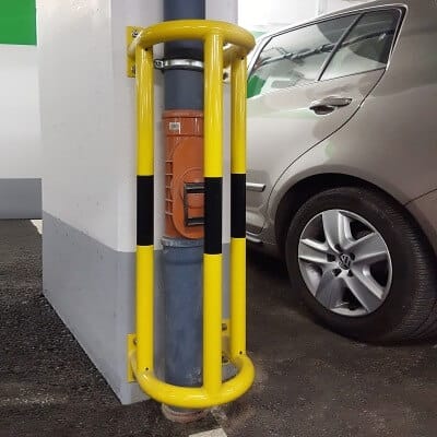 Gelber MORION Rohrschutz 180° für Wandmontage sichert senkrechtes Rohr und orange Elektrobox neben silbernem Auto in Tiefgarage.