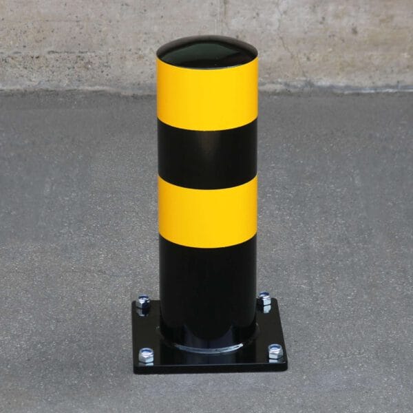 Schwarzer Rammschutz-Poller aus Metall mit zwei gelben Reflexstreifen auf Betonboden vor rauer Betonwand, LKW Parkhilfe.