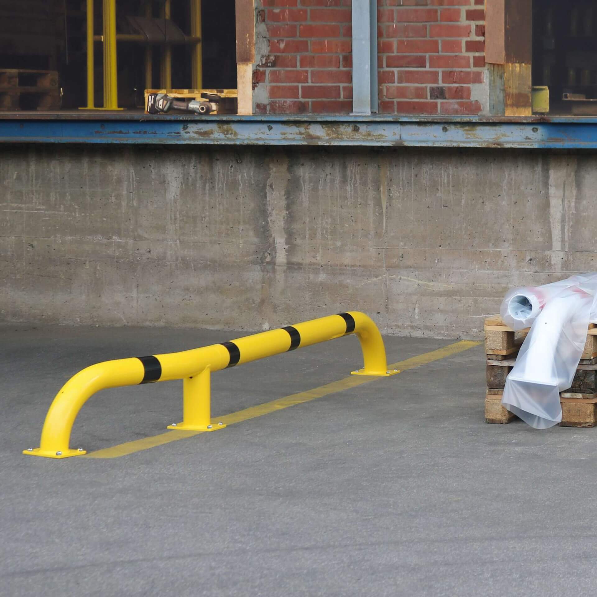 BLACK BULL LKW-Einfahrhilfe gelb-schwarz, installiert vor Verladerampe, gestapelte Paletten, Betonwand im Hintergrund.