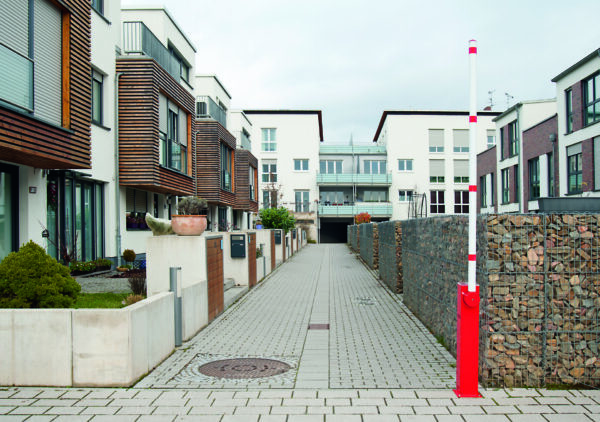 Moderne Wohnanlage mit weißen Gebäuden, Balkonen und Gehweg; rote COMPACT Elektroschranke mit Solarmodul angehoben.