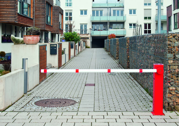 COMPACT Elektroschranke mit Solarmodul sperrt Zufahrt zu Wohnstraße mit modernen Apartments und Natursteinmauern.