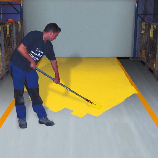 Person markiert industriellen Lagerhallenboden mit gelber PROline-paint Hallenmarkierfarbe und Farbroller.