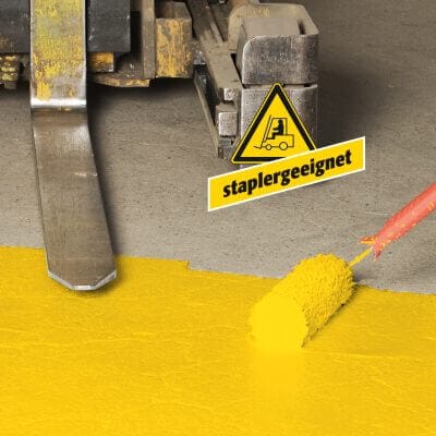 Boden wird mit gelber PROline Antirutsch Hallenmarkierfarbe per Roller markiert, Warnschild "staplergeeignet" steht daneben.