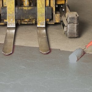 Ein Farbroller trägt graue Antirutsch-Bodenmarkierungsfarbe auf Betonboden vor Gabelstapler auf. Hallenmarkierung sichtbar.
