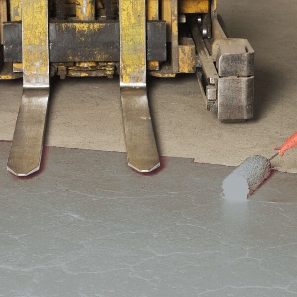 Ein Farbroller trägt graue Antirutsch-Bodenmarkierungsfarbe auf Betonboden nahe gelber Gabelstaplergabeln auf.