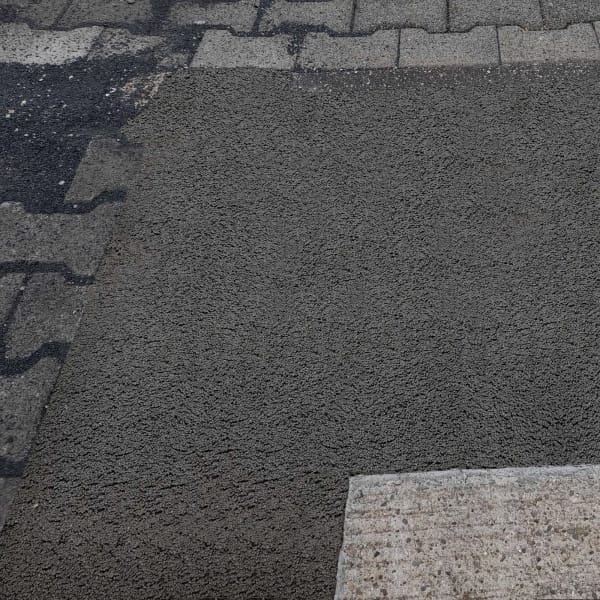 Asphalt verbindet nahtlos neue Fahrbahndecke mit alten Pflastersteinen und Betonslab auf der Straße. Bodenreparatur sichtbar.