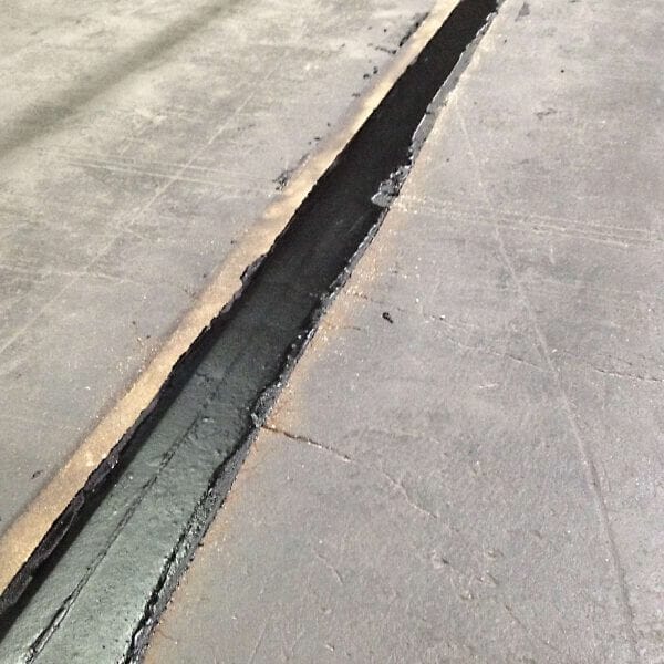 Breiter Riss im Betonboden, ausgefüllt mit schwarzem Restore Fugenreparatur-Dichtstoff, gut sichtbar auf grauem Beton.