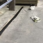 Ein schmaler Streifen Restore Fugenreparatur auf Betonboden, daneben ein Handschuh-Stapel und ein weißer Eimer.
