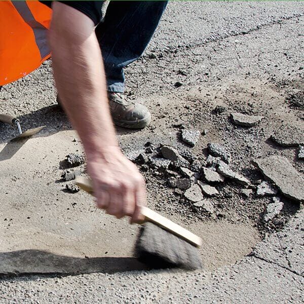 Eine Person kehrt mit Restore Bodenreparatur loses Material aus einem Schlagloch auf einer Asphaltstraße zur Reparaturvorbereitung.