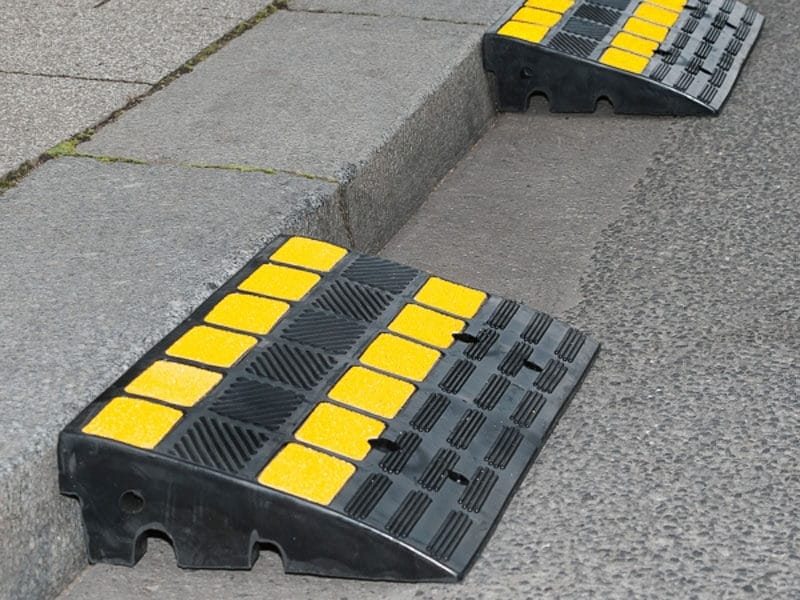 Zwei schwarz-gelbe MORION Bordsteinrampen am Gehwegrand ermöglichen rollstuhlgerechten Übergang zwischen Gehweg und Straße.