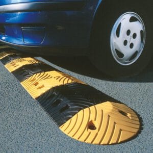 Nahaufnahme eines Autoreifens überfährt gelb-schwarze TOPSTOP Fahrbahnschwelle Kautschuk auf Asphaltstraße.